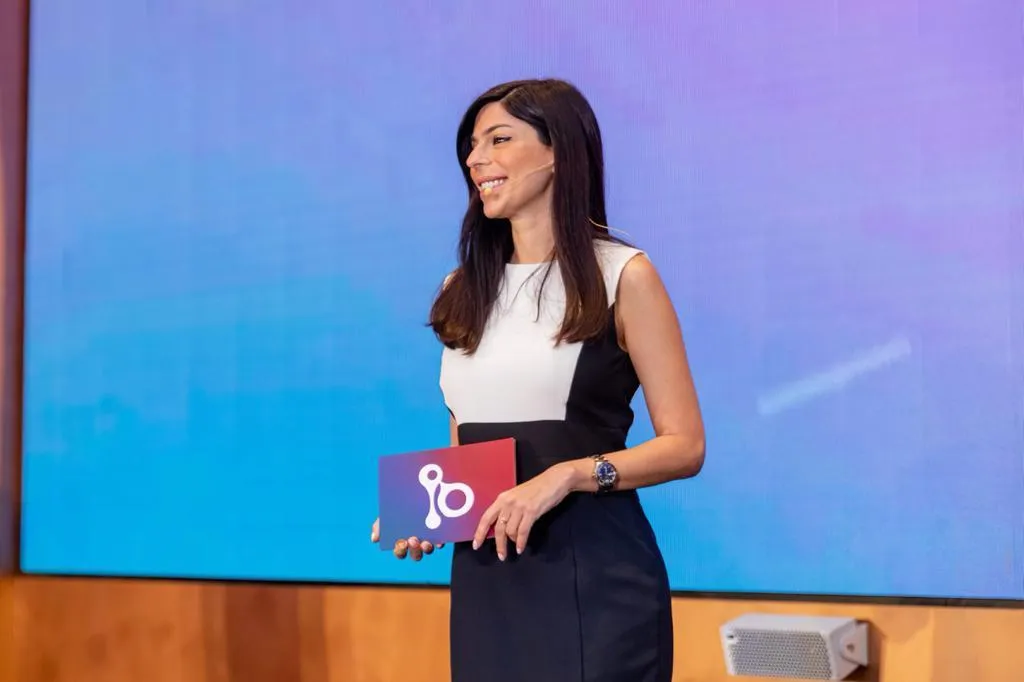 Rima Iskandarani hosting a corporate event in a colorblock dress, presenting in front of a large screen