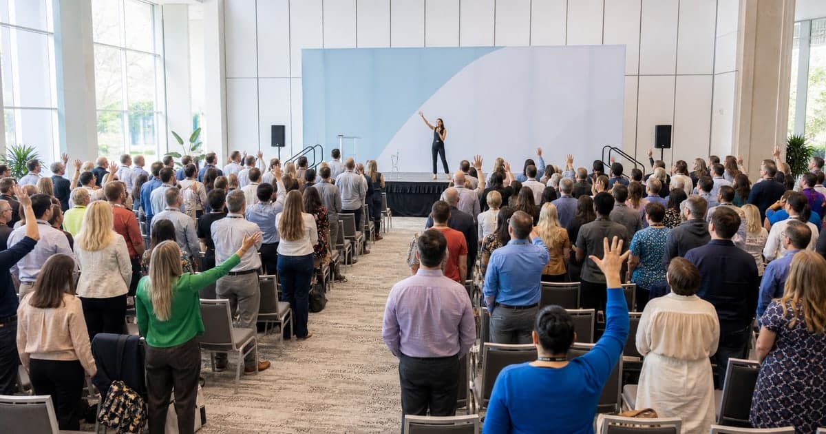 Large conference audience standing and responding together as the host resets the room after lunch