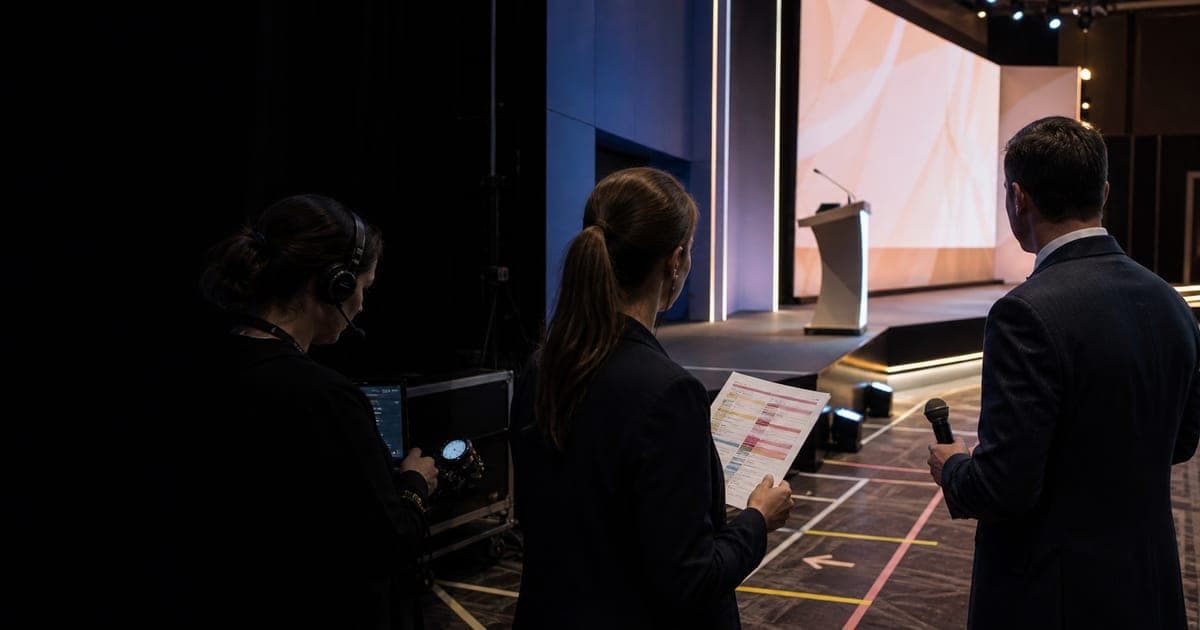 Host, planner, and stage manager reviewing a run sheet beside an empty event stage